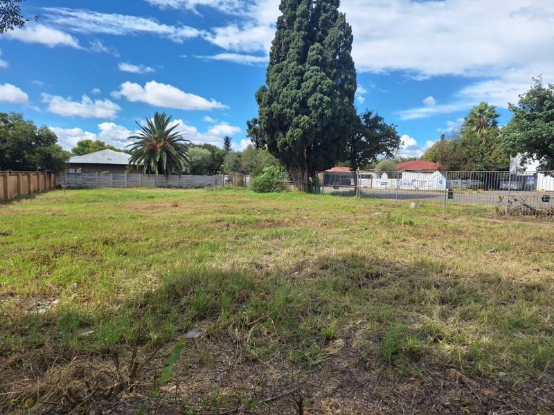 A vacant commercial land plot featuring established trees, grassed terrain, and perimeter fencing, offering a clear space for potential development.