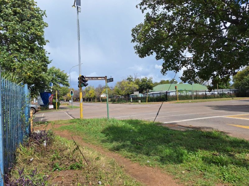 A street-level view of a commercial intersection featuring traffic signals, street signage, and surrounding perimeter fencing.