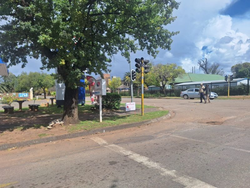 A street-level view of a commercial intersection featuring traffic signals, paved road infrastructure, and mature landscaping.