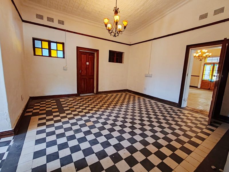 Spacious room featuring classic checkerboard tile flooring, a decorative pressed metal ceiling, and a vintage chandelier, offering a character-filled blank canvas.