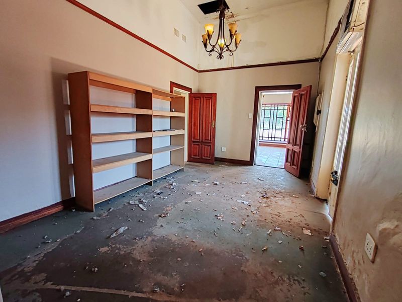 A vacant office space featuring timber doors and a ceiling light fixture, currently requiring significant maintenance and flooring repairs.