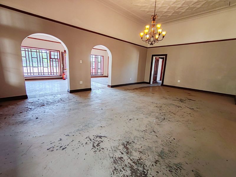 Spacious living area featuring arched doorways, decorative ceiling details, and a chandelier, currently requiring significant floor restoration.