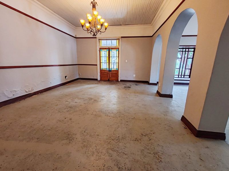 Spacious living area featuring arched architectural details, a stained glass entrance door, and a classic chandelier, currently awaiting renovation and flooring updates.