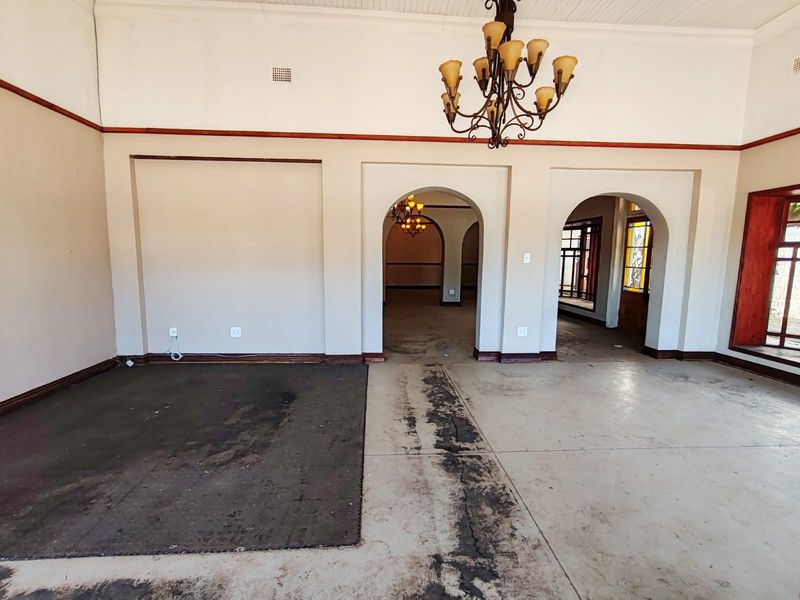 Spacious living area featuring classic arched doorways, a decorative chandelier, and original architectural details, currently requiring flooring restoration and cosmetic updates.