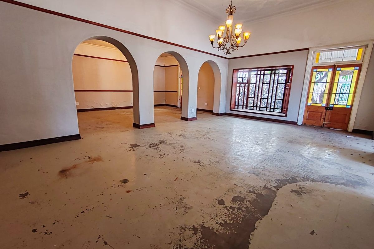 Spacious living area featuring classic arched architectural details, a stained glass entrance door, and a decorative chandelier, requiring floor and wall refinishing.