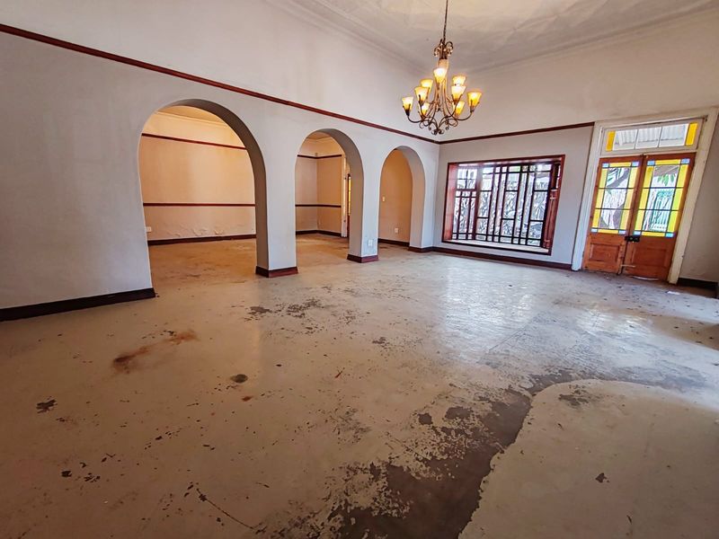 Spacious living area featuring classic arched architectural details, a stained glass entrance door, and a decorative chandelier, requiring floor and wall refinishing.