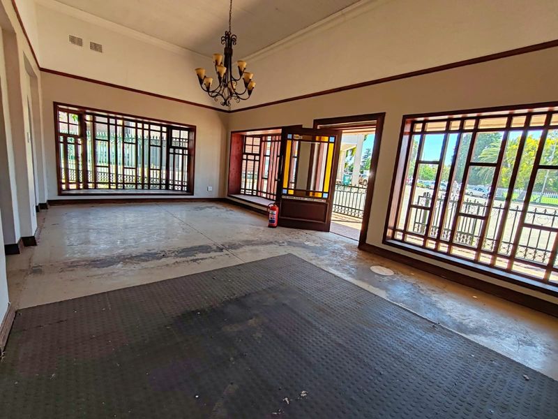 Spacious, empty living area featuring large timber-framed windows with security bars, a decorative chandelier, and a characterful stained glass entrance door.