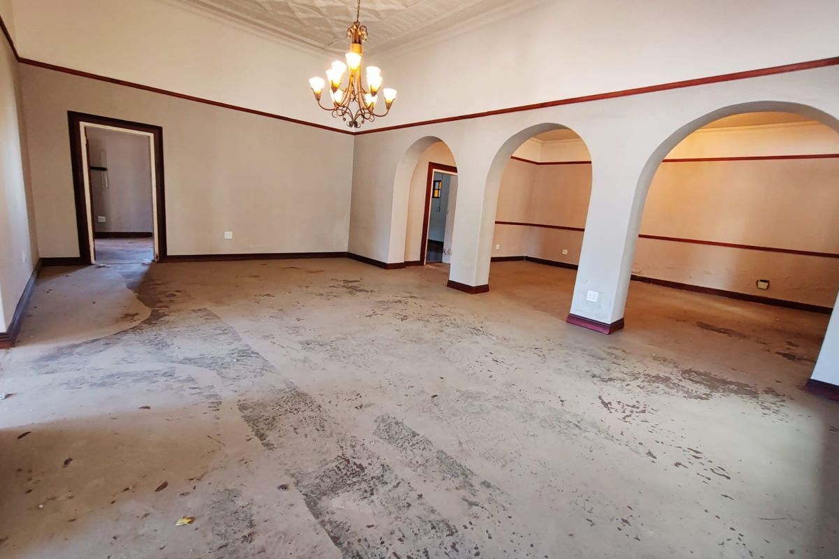 Spacious, empty living area featuring classic arched doorways, a decorative ceiling, and a central chandelier, offering a blank canvas for renovation.