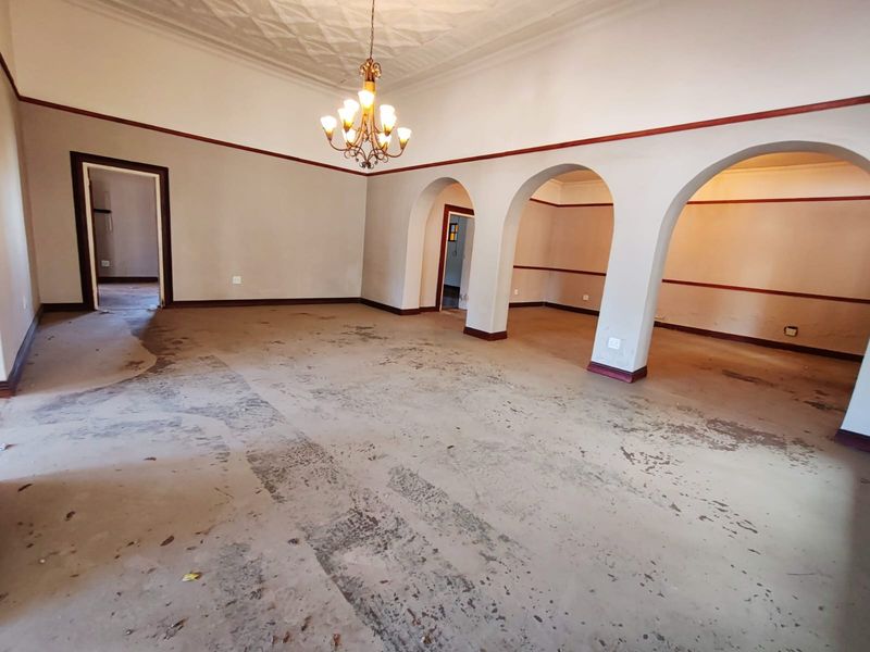 Spacious, empty living area featuring classic arched doorways, a decorative ceiling, and a central chandelier, offering a blank canvas for renovation.