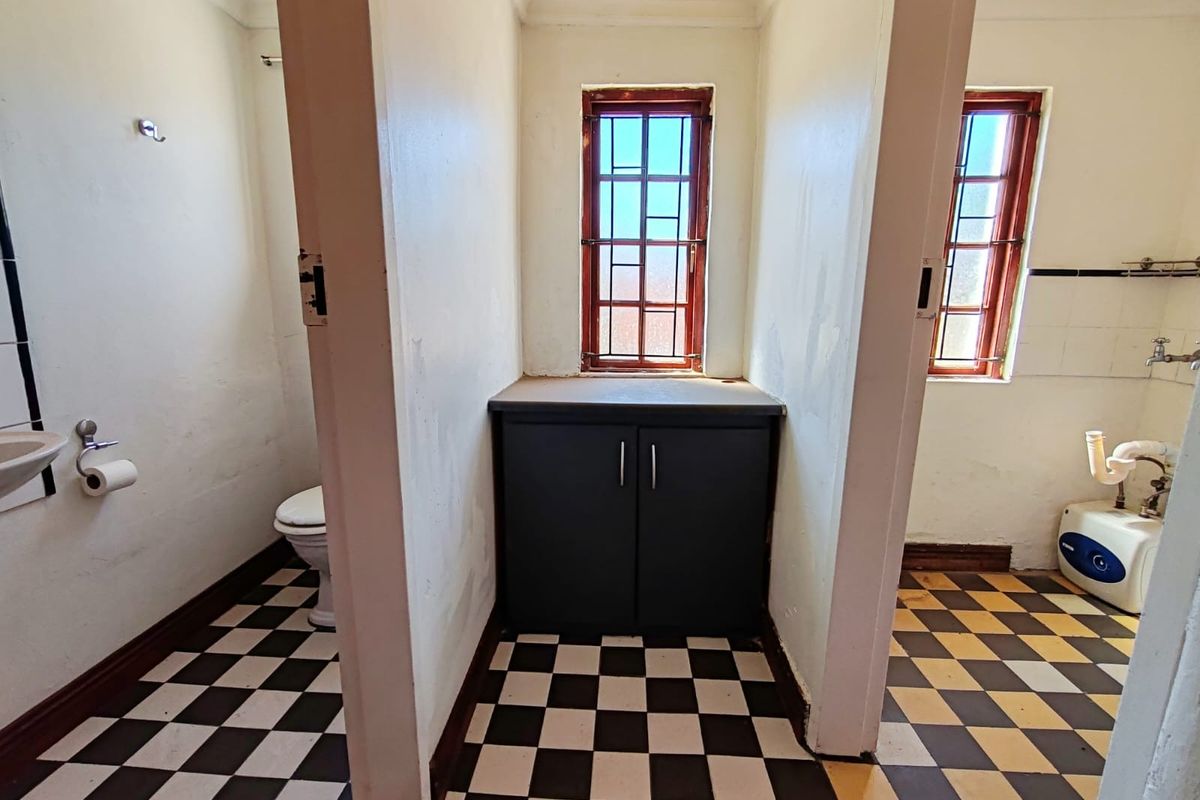 A dated bathroom featuring a partitioned layout, checkered floor tiles, built-in vanity storage, and basic sanitary fixtures in need of cosmetic refurbishment.