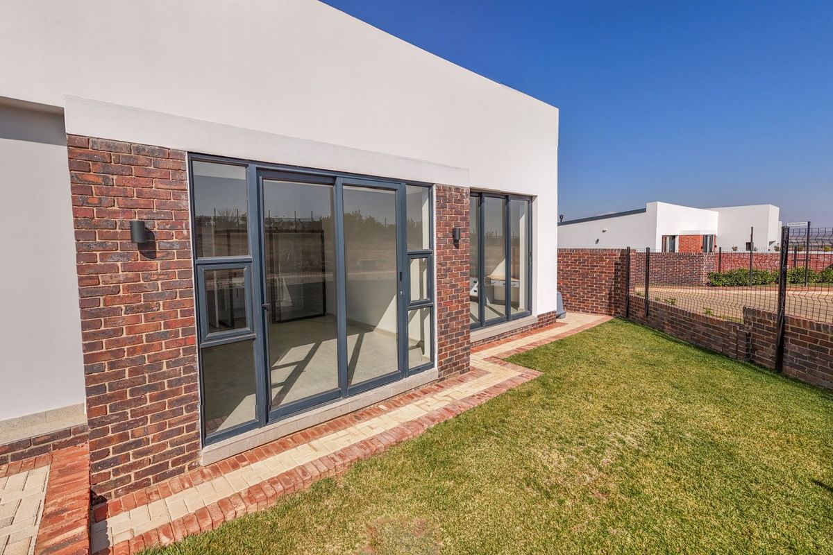 Rear view of the property featuring a modern brick facade, large sliding glass doors, a paved walkway, and a well-maintained lawn.