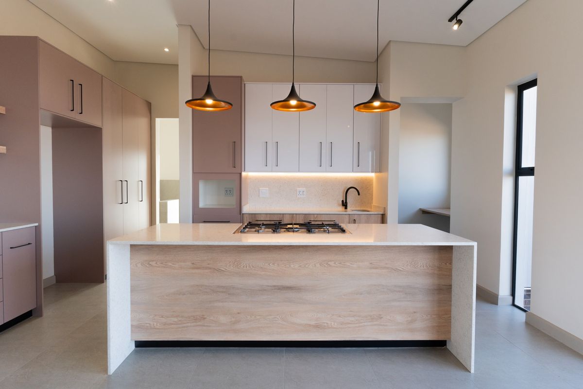Modern kitchen featuring a central island with a gas hob, sleek cabinetry, stone countertops, and contemporary pendant lighting in a bright, open space.