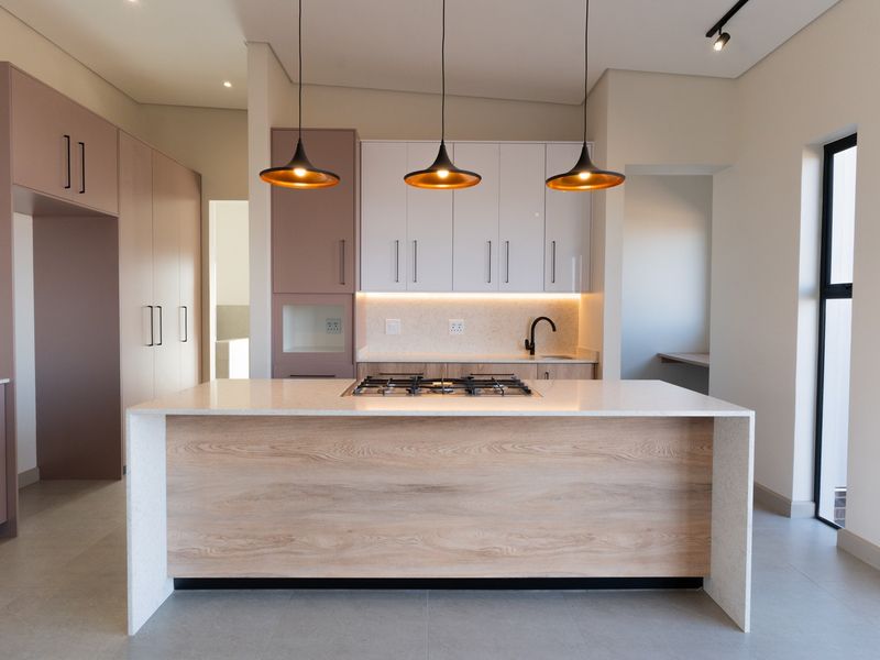 Modern kitchen featuring a central island with a gas hob, sleek cabinetry, stone countertops, and contemporary pendant lighting in a bright, open space.