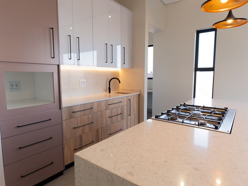 Modern kitchen featuring two-tone cabinetry, stone countertops, a central island with a gas hob, and integrated lighting.