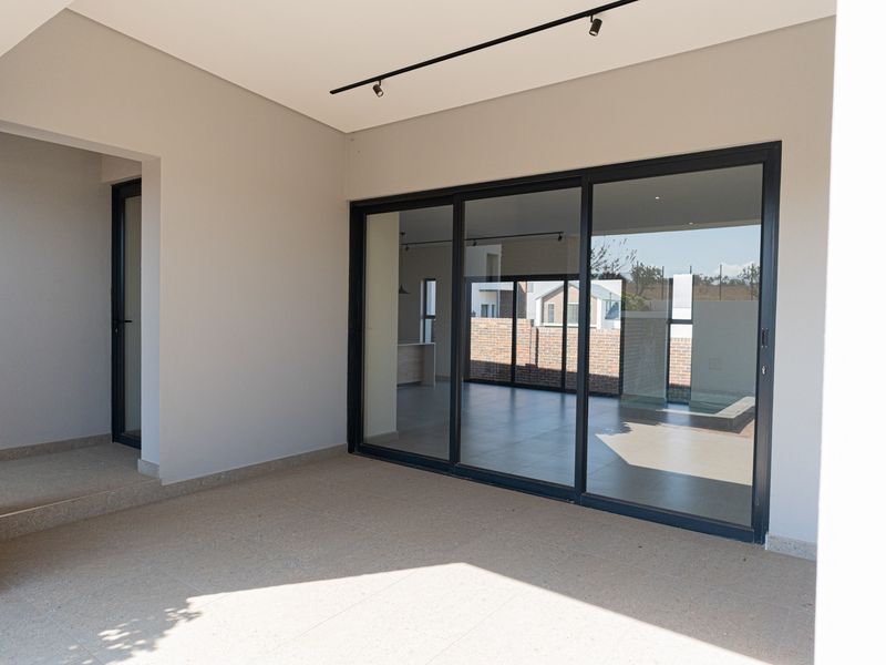 A modern covered patio featuring tiled flooring, track lighting, and large sliding glass doors providing seamless access to the interior living space.