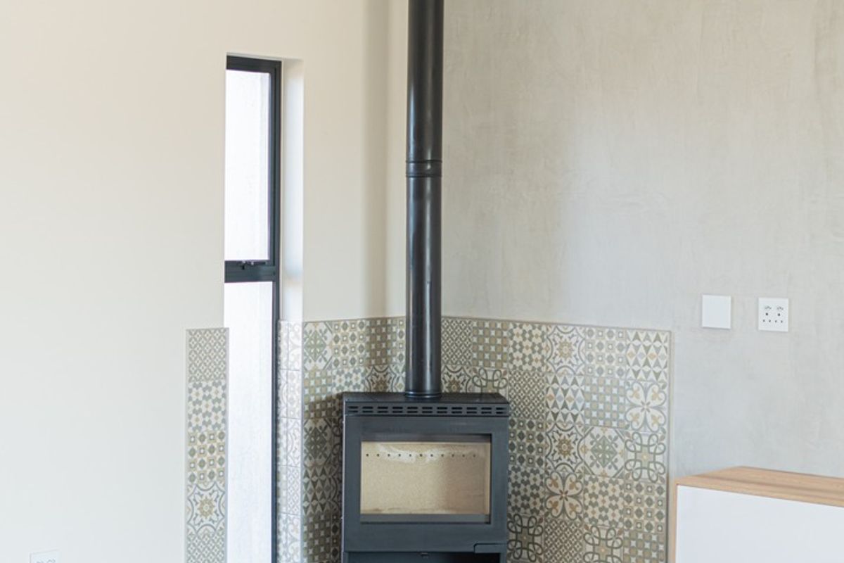 A bright, modern living area featuring a sleek black freestanding fireplace with decorative patterned tiling and a wall-mounted air conditioning unit.