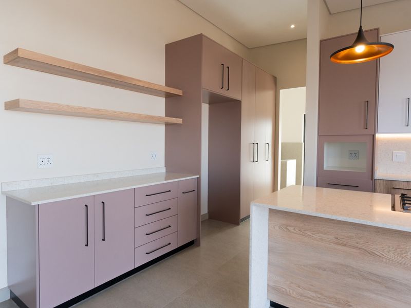 Modern kitchen featuring soft-toned cabinetry, stone countertops, integrated gas hob, and floating timber shelving in a clean, contemporary design.