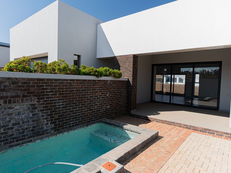 A modern outdoor area featuring a compact plunge pool, paved patio space, and a brick boundary wall, adjacent to the main living area.