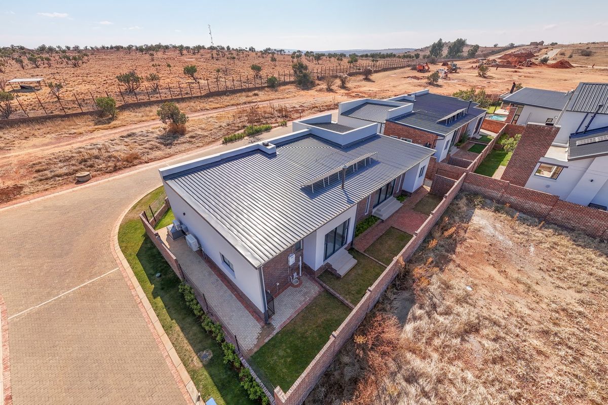 Aerial view of a modern residential property featuring a metal roof, brick boundary walls, and paved driveway in a developing estate setting.