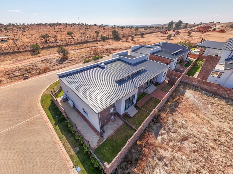Aerial view of a modern residential property featuring a metal roof, brick boundary walls, and paved driveway in a developing estate setting.