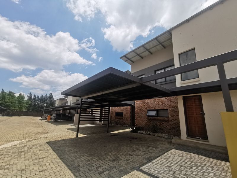 Front exterior view of a modern townhouse featuring a paved driveway, covered carport, and a combination of brick and plastered wall finishes.