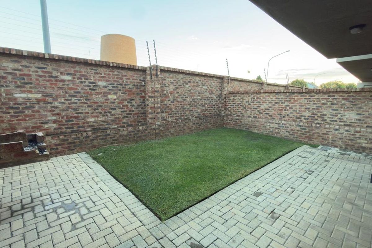A private rear courtyard featuring a paved patio, artificial lawn, and a built-in brick braai, enclosed by high brick walls with electric fencing.