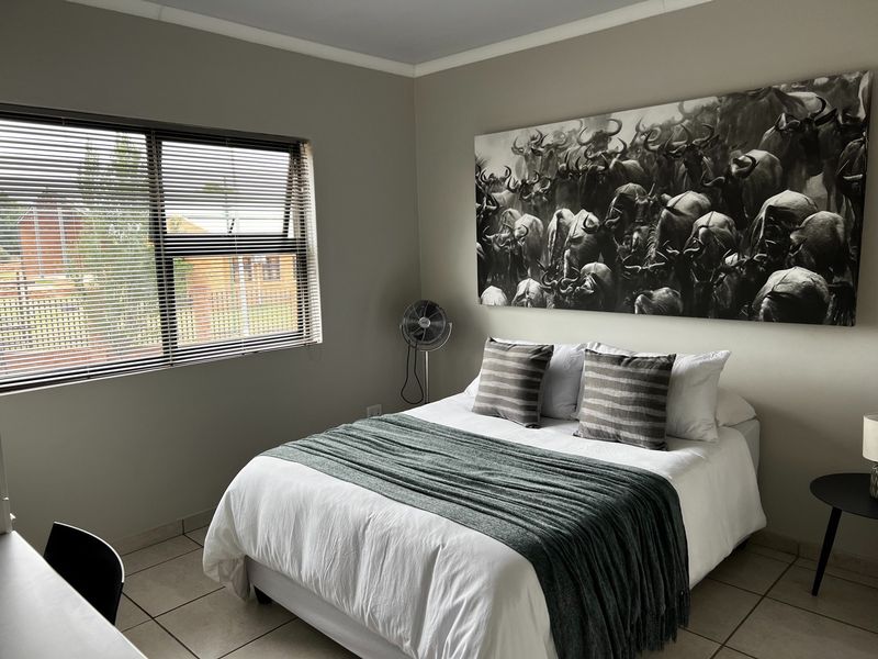 A well-maintained bedroom featuring neutral wall tones, tiled flooring, and a functional top-hung window with fitted horizontal blinds.