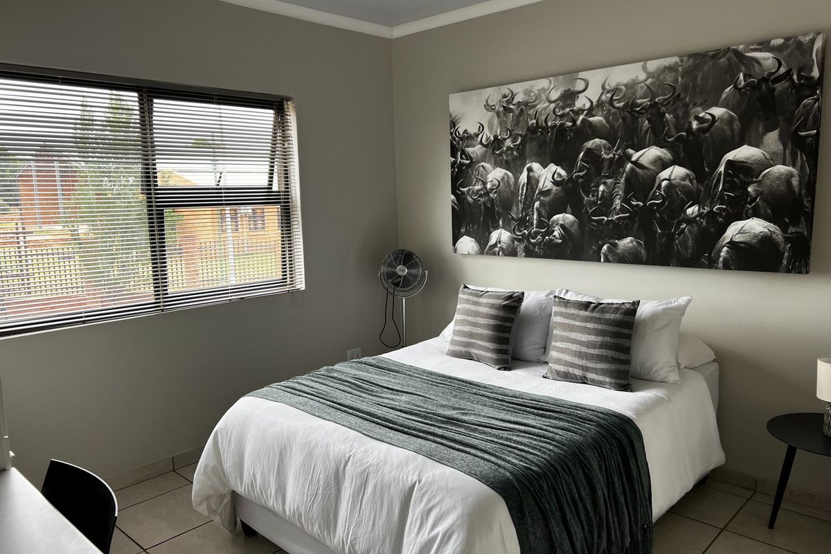 A well-maintained bedroom featuring neutral wall tones, tiled flooring, and a functional top-hung window with fitted horizontal blinds.