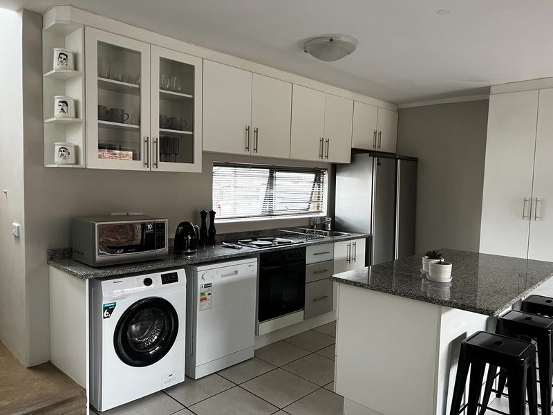 Modern kitchen featuring granite countertops, ample cabinetry, a central island, and integrated appliance spaces, finished with neutral tones and tiled flooring.