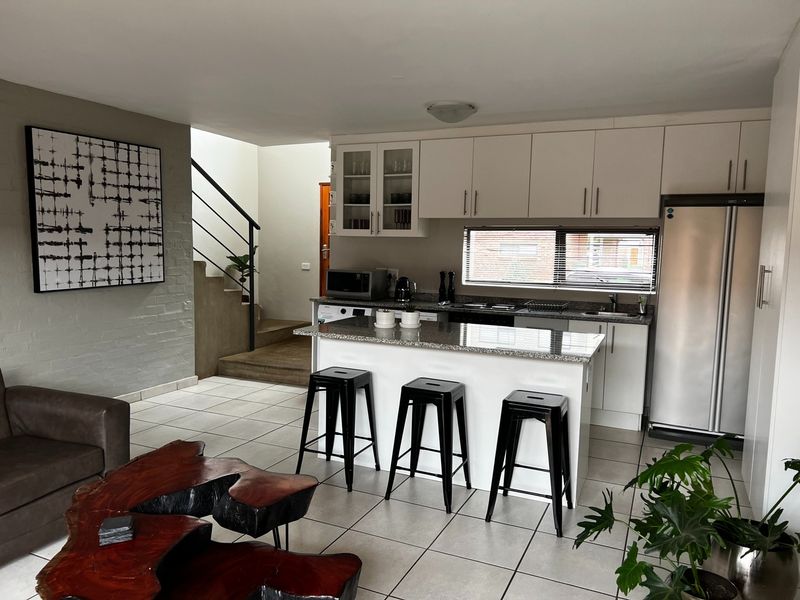 Open-plan living area featuring a modern kitchen with granite countertops, white cabinetry, and a staircase leading to the upper level.