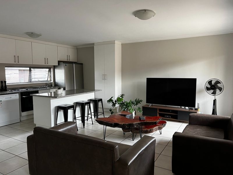 Open-plan living area featuring a modern kitchen with granite countertops, built-in cabinetry, and tiled flooring throughout the combined kitchen and lounge space.