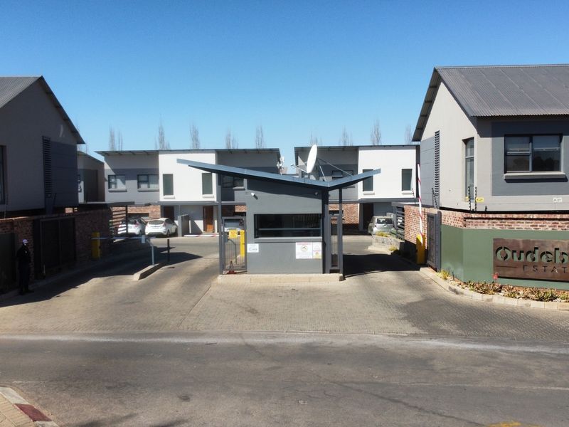 The entrance to Oudebrug Estate featuring a modern security gatehouse, boom gate access, and well-maintained brick and plaster townhouse facades.