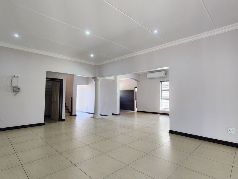 Spacious open-plan living area featuring neutral tiled flooring, recessed lighting, and a wall-mounted air conditioning unit, offering a versatile and well-maintained interior space.