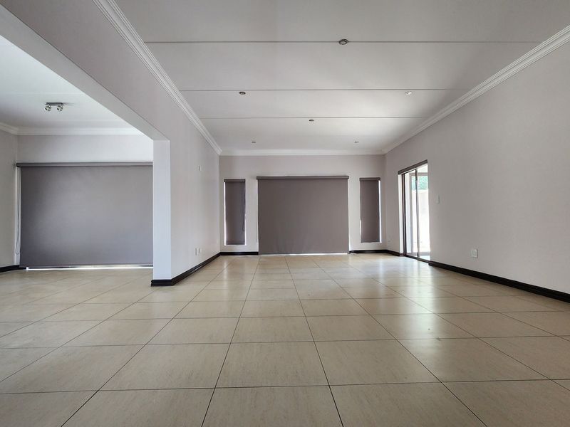 A spacious, empty open-plan living area featuring neutral tiled flooring, recessed ceiling lights, and modern roller blinds, offering a clean and versatile blank canvas.