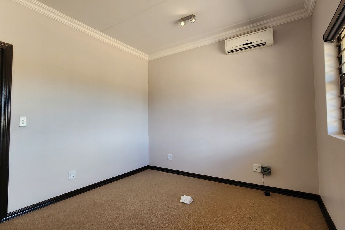 A clean, empty bedroom featuring neutral walls, carpeted flooring, crown molding, and a wall-mounted air conditioning unit.