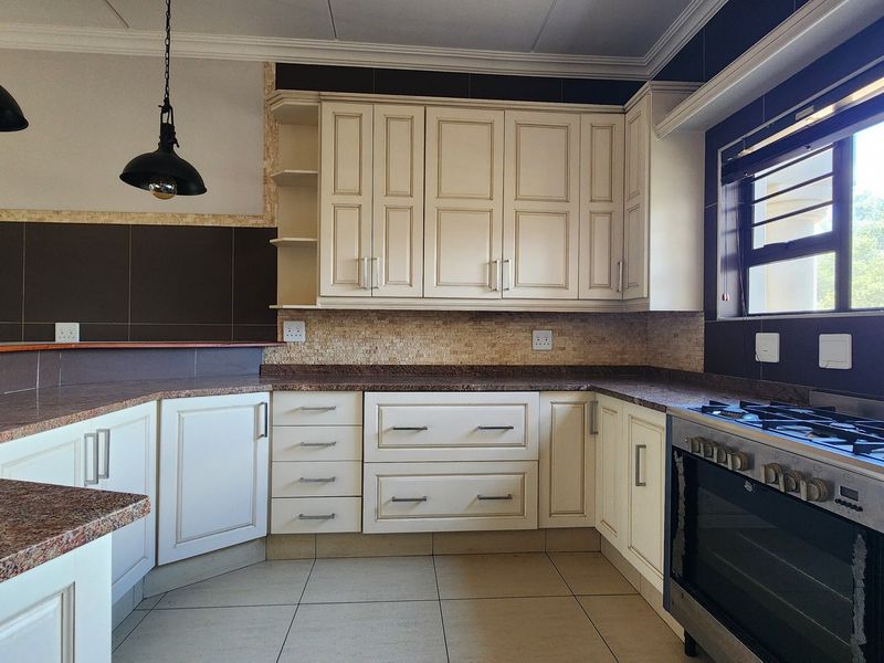 A well-maintained kitchen featuring cream-colored cabinetry, granite countertops, a gas stove with oven, and tiled flooring with modern pendant lighting.