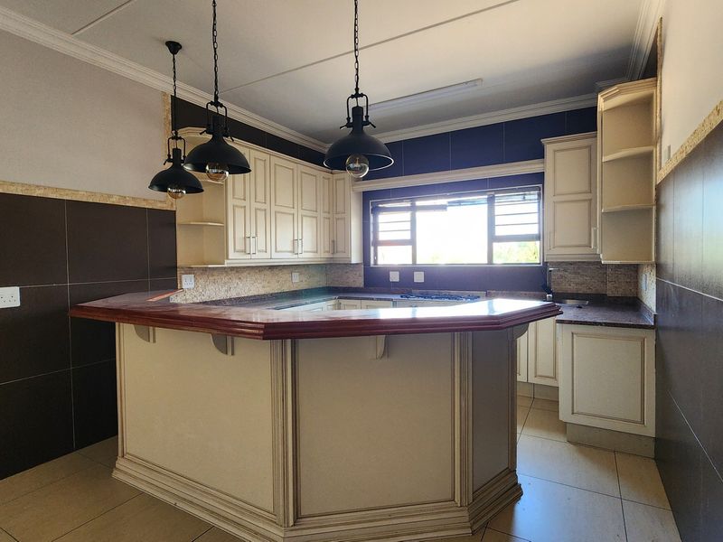 A spacious kitchen featuring cream cabinetry, a large breakfast bar, dark tiled splashbacks, and modern pendant lighting, offering a functional and well-defined prep area.