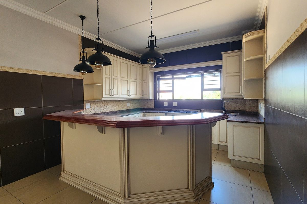 A spacious kitchen featuring cream cabinetry, a large breakfast bar, dark tiled splashbacks, and modern pendant lighting, offering a functional and well-defined prep area.