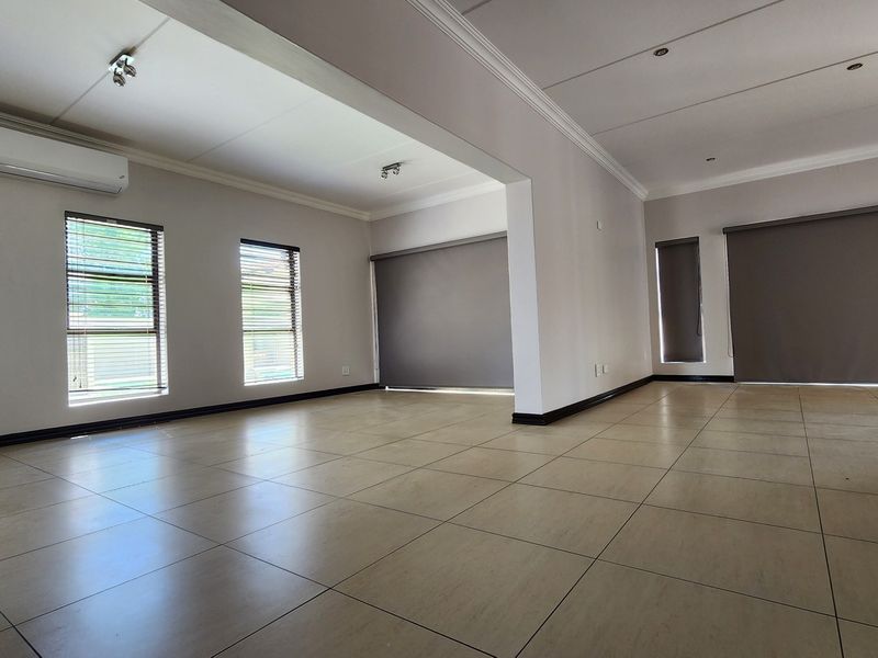 Spacious, light-filled open-plan living area featuring neutral tiled flooring, modern downlighting, and split-system air conditioning.