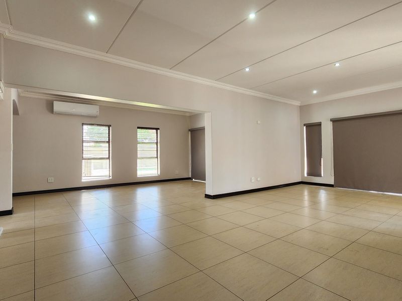 Spacious open-plan living area featuring neutral ceramic floor tiles, recessed downlighting, a decorative column, and split-system air conditioning.