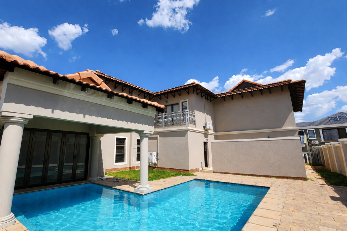 Rear view of the property featuring a swimming pool, covered patio area, and a balcony with decorative metal railing under a clear blue sky.