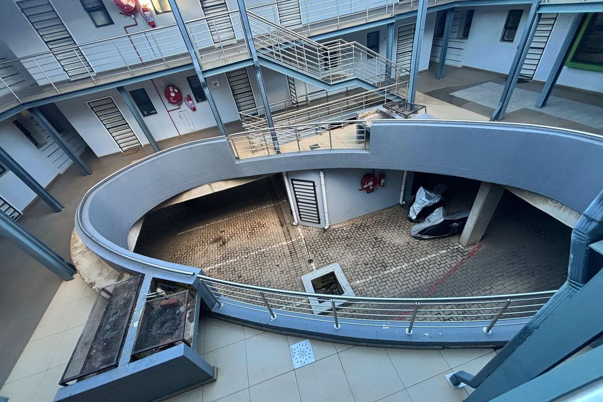 An elevated view of an apartment complex courtyard featuring a paved parking area, metal staircases, and a built-in braai facility.