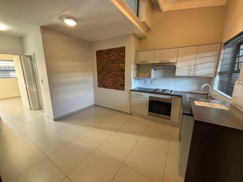 Open-plan kitchen and living area featuring tiled floors, built-in cabinetry with integrated appliances, and a decorative exposed brick feature wall.