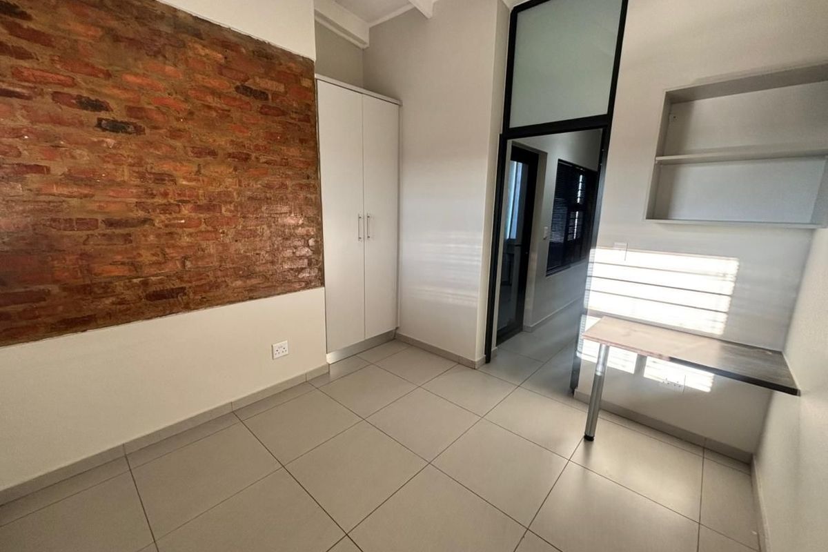 A bright bedroom featuring an exposed brick accent wall, tiled flooring, built-in storage, and a functional built-in desk area.