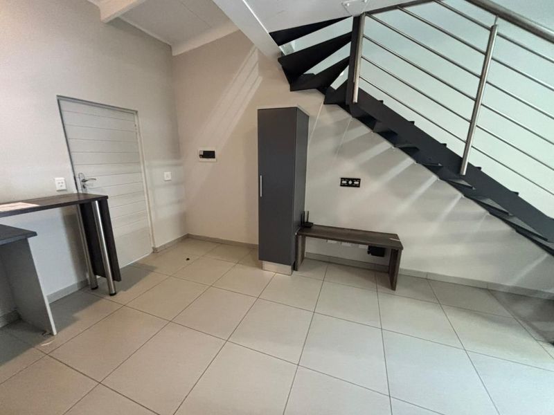An open-plan living area featuring modern tiled flooring and a striking staircase with a metal balustrade, offering a clean and contemporary aesthetic.