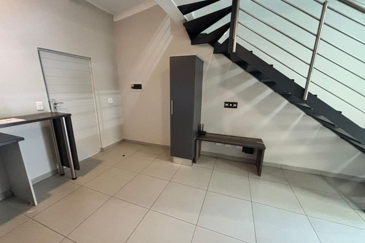 An open-plan living area featuring modern tiled flooring and a striking staircase with a metal balustrade, offering a clean and contemporary aesthetic.