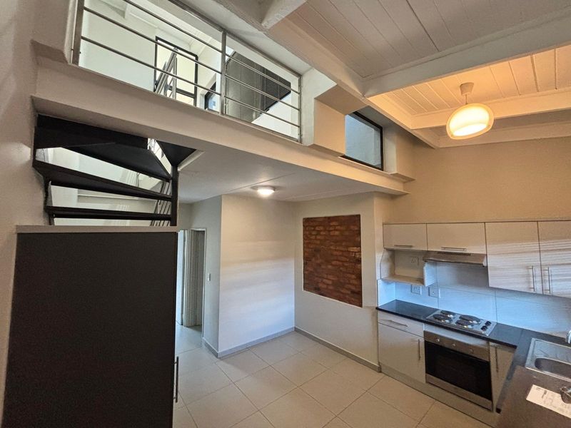 Open-plan kitchen and living area featuring a mezzanine level, spiral staircase, exposed brickwork, and modern built-in cabinetry with integrated appliances.