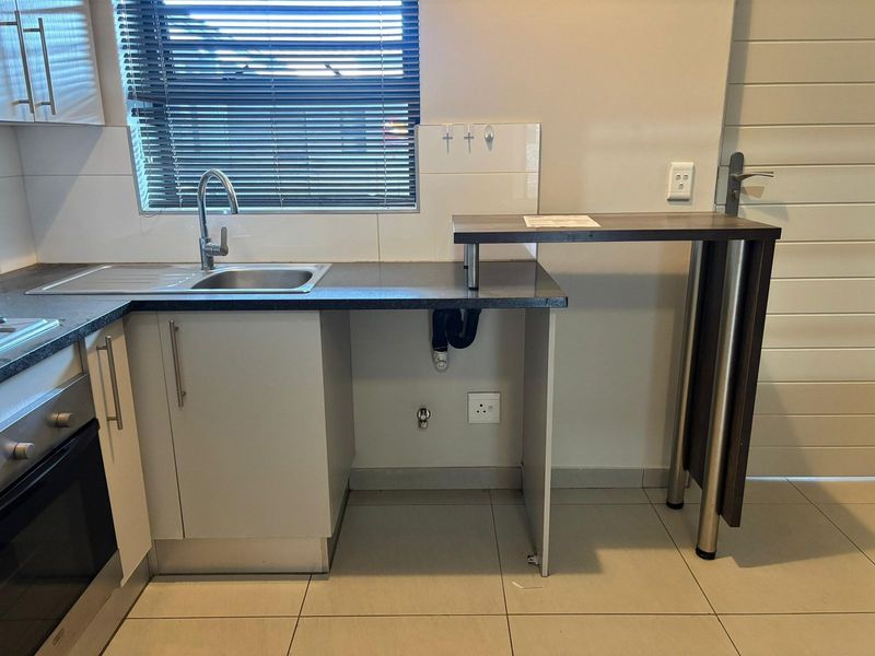 A functional kitchen area featuring built-in cabinetry, a stainless steel sink, integrated oven and hob, and a breakfast bar counter.