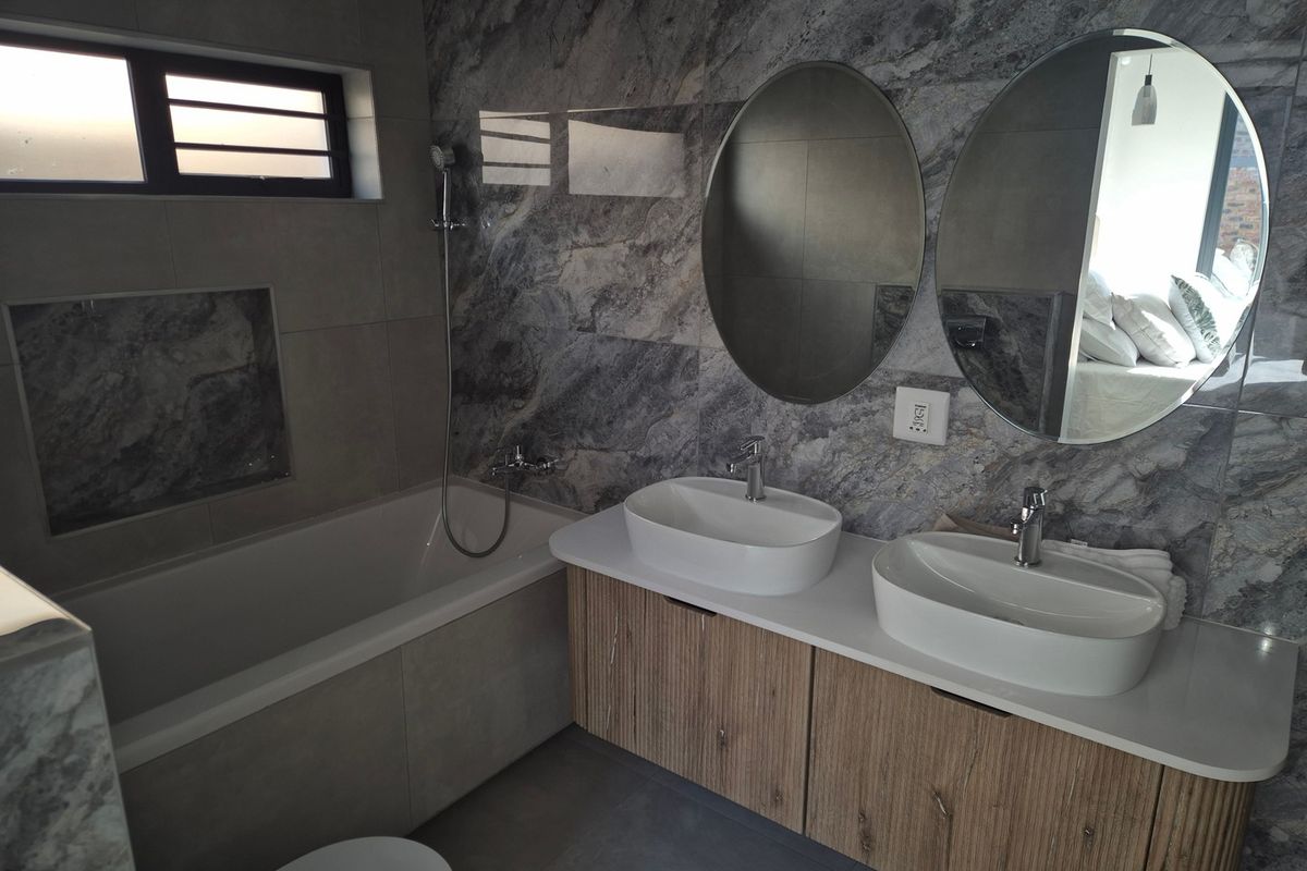 Modern bathroom featuring a double vanity with vessel sinks, a built-in bathtub with handheld shower, and contemporary marble-effect wall tiling.