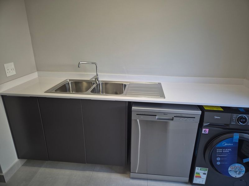 A modern, clean laundry area featuring sleek dark cabinetry, a white quartz countertop, and a stainless steel double sink with a chrome mixer tap.